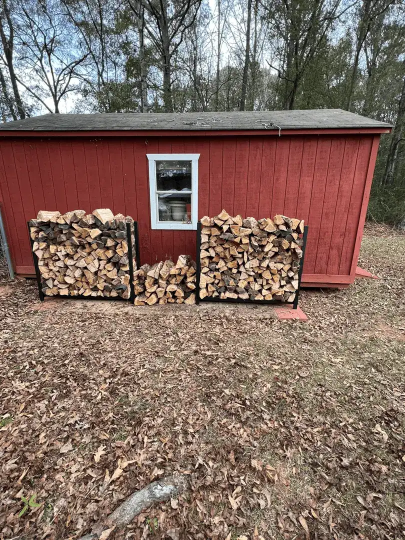 Two stacks of firewood beside a red shed